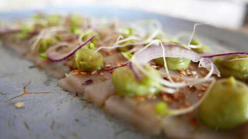Thin slices of cliff fish on blue plate, decorated with sliced red onion, avokadopurrée, and water