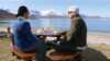 Two persons sitting by a outdoor table looking at the fjord and the mountains