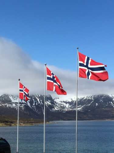 Tre flaggstenger med norske flagg til tops på alle tre