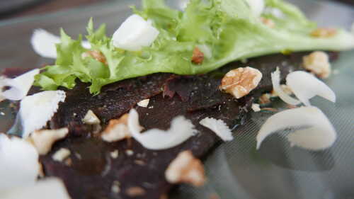 Whale carpassio on plate with chopped walnuts, white goat chees, and green salad